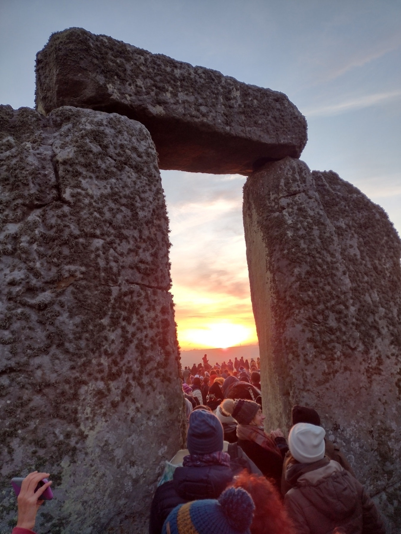 People gather at an ancient stone structure to watch the sunrise.