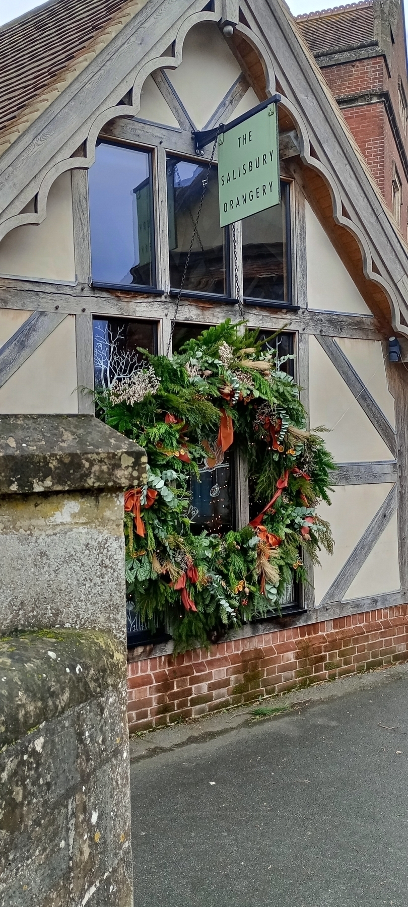 A large festive wreath decorates the exterior of a building with Tudor-style architecture, displaying a sign that reads The Salisbury Orangery.